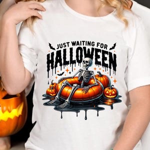 May include: White t-shirt with a graphic of a skeleton in a pumpkin-shaped pool float. The text "Just Waiting for Halloween" is above the skeleton.