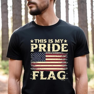 Puede incluir: Una camiseta negra con un dise&ntilde;o de bandera estadounidense desgastado y el texto "This is my pride flag".