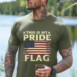 Puede incluir: Una camiseta verde con un gr&aacute;fico de bandera estadounidense desgastado y el texto "This is my pride flag".