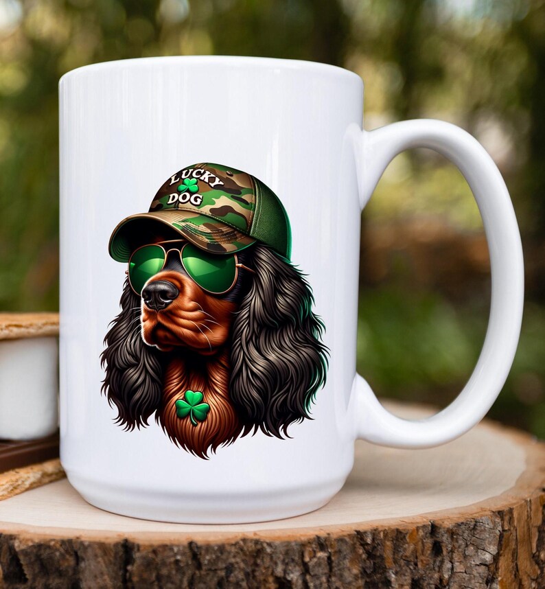 May include: White ceramic mug with a graphic of a black and brown dog wearing a camouflage hat with the text "Lucky Dog" and green sunglasses. The dog is wearing a green shamrock necklace.