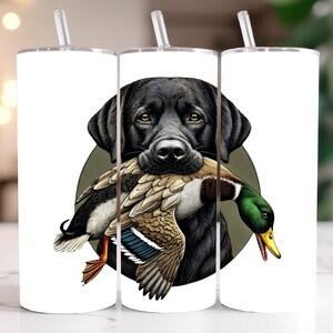 Pu&ograve; includere: Bicchiere bianco con una grafica di un Labrador Retriever nero che tiene un'anatra. L'anatra ha piume marroni, bianche e verdi. Il bicchiere ha un coperchio argentato e una cannuccia trasparente. Le parole "DIGITAL DOWNLOAD" sono stampate sul lato.