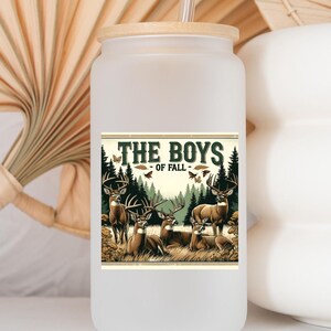 K&ouml;nnte beinhalten: Ein wei&szlig;er, mattierter Becher mit Bambusdeckel und Strohhalm. Der Becher zeigt eine Grafik mit f&uuml;nf Hirschen in einem Wald mit dem Text "The Boys of Fall".