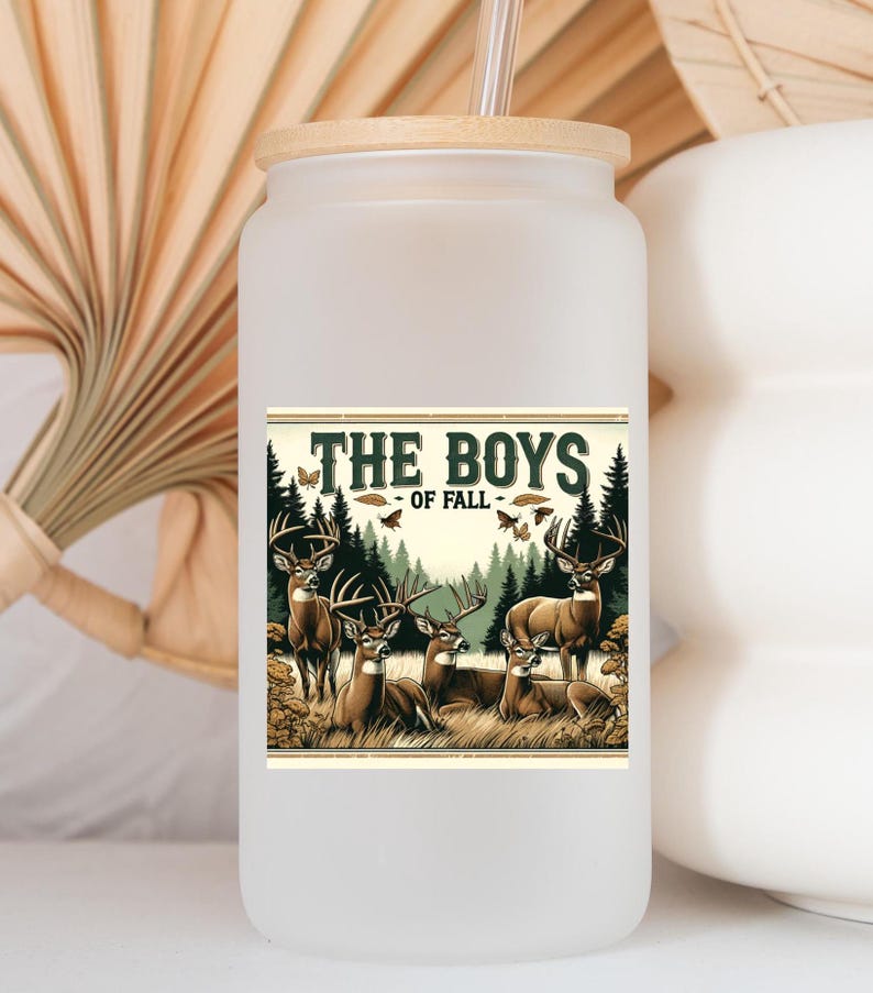 K&ouml;nnte beinhalten: Ein wei&szlig;er, mattierter Becher mit Bambusdeckel und Strohhalm. Der Becher zeigt eine Grafik mit f&uuml;nf Hirschen in einem Wald mit dem Text "The Boys of Fall".