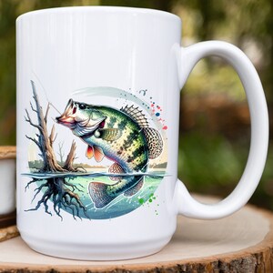 May include: White ceramic coffee mug with a colorful illustration of a green and brown fish jumping out of the water. The fish is surrounded by blue, green, and red watercolor splatters.