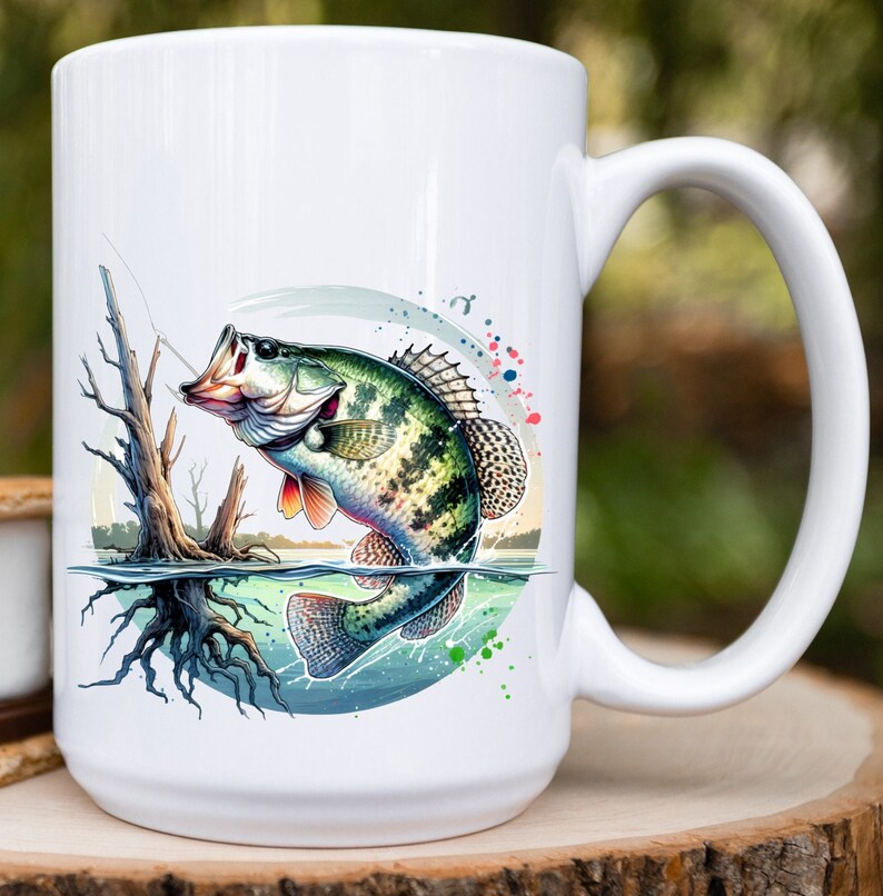 May include: White ceramic coffee mug with a colorful illustration of a green and brown fish jumping out of the water. The fish is surrounded by blue, green, and red watercolor splatters.
