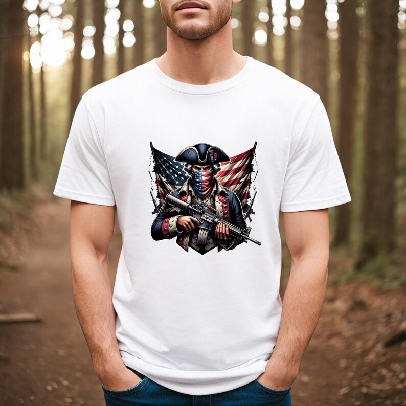 May include: White t-shirt with a graphic of a man wearing a tri-cornered hat and bandana, holding a rifle, with an American flag behind him.