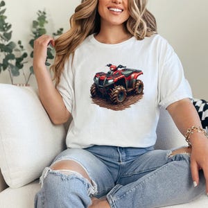 May include: White t-shirt featuring a graphic of a red and black ATV. The ATV has large, rugged tires and is depicted on a brown, dirt-like surface. The shirt is a casual style, with a relaxed fit.