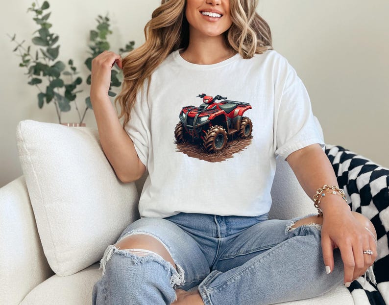 May include: White t-shirt featuring a graphic of a red and black ATV. The ATV has large, rugged tires and is depicted on a brown, dirt-like surface. The shirt is a casual style, with a relaxed fit.