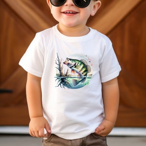 May include: White toddler t-shirt with a colorful graphic of a bass fish jumping out of the water. The fish is green, brown, and black with a white belly. The background is a blue circle with white and green splashes of paint.