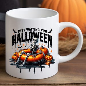May include: White ceramic coffee mug with a black and white illustration of a skeleton sitting in a pumpkin-shaped float. The text "Just Waiting for Halloween" is written in black dripping letters above the skeleton.