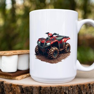 May include: White ceramic mug featuring a red ATV graphic. The ATV is detailed with black accents and sits on a muddy ground illustration. The mug has a large handle and is set on a wooden surface.