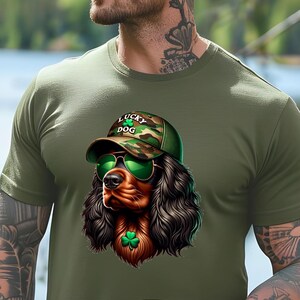 May include: A green t-shirt with a cartoon image of a brown and black dog wearing a camouflage baseball cap with the text "Lucky Dog" and green sunglasses. The dog is wearing a green shamrock around its neck.