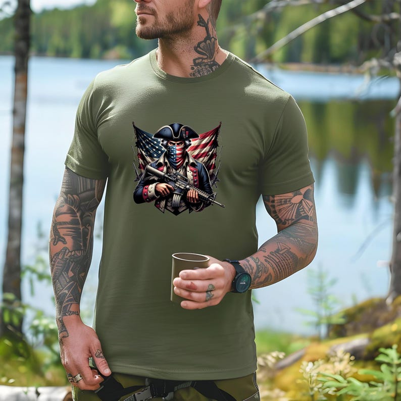 May include: A green t-shirt with a graphic of a person wearing a bandana and a tri-cornered hat holding a rifle. The person is standing in front of an American flag.
