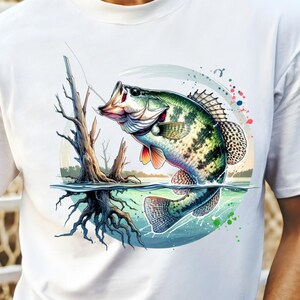 May include: A white t-shirt with a colorful illustration of a largemouth bass jumping out of the water. The fish is green, white, and black with red fins. The background is a blue and green watercolor design with a tree trunk and roots.