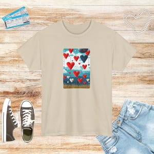 Peut inclure: Un t-shirt beige avec un imprimé graphique de cœurs rouges et bleus flottant dans le ciel. Les cœurs sont attachés à des ficelles et sont disposés de manière aléatoire.