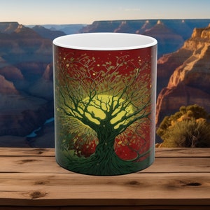 Peut inclure: Mug en céramique blanche avec une illustration détaillée d'un arbre et d'un soleil jaune. L'arbre a des feuilles et des branches vertes sur un fond rouge. La tasse est posée sur une surface en bois avec un arrière-plan panoramique.