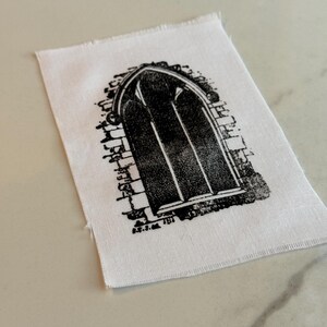 May include: Black and white iron-on patch featuring a detailed illustration of an arched window with a brick frame.