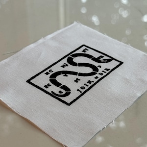 May include: A white fabric patch with a black snake design and the text "Don't Tread On Me" in a black rectangle.