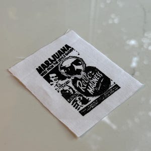 May include: White fabric patch with black text and graphic. The text reads "MARIJUANA WEED FROM THE DEVIL'S GARDEN" and "Rebel Madness".