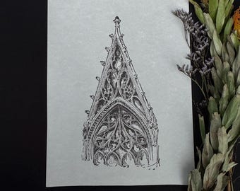 May include: A black and white architectural drawing of a gothic archway on textured paper. The detailed illustration features intricate tracery and a pointed top. Dried flowers and foliage are arranged on a black surface near the drawing.