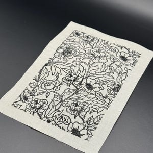 Puede incluir: Una tela blanca con un estampado floral negro impreso en ella. El patr&oacute;n presenta una variedad de flores y hojas.