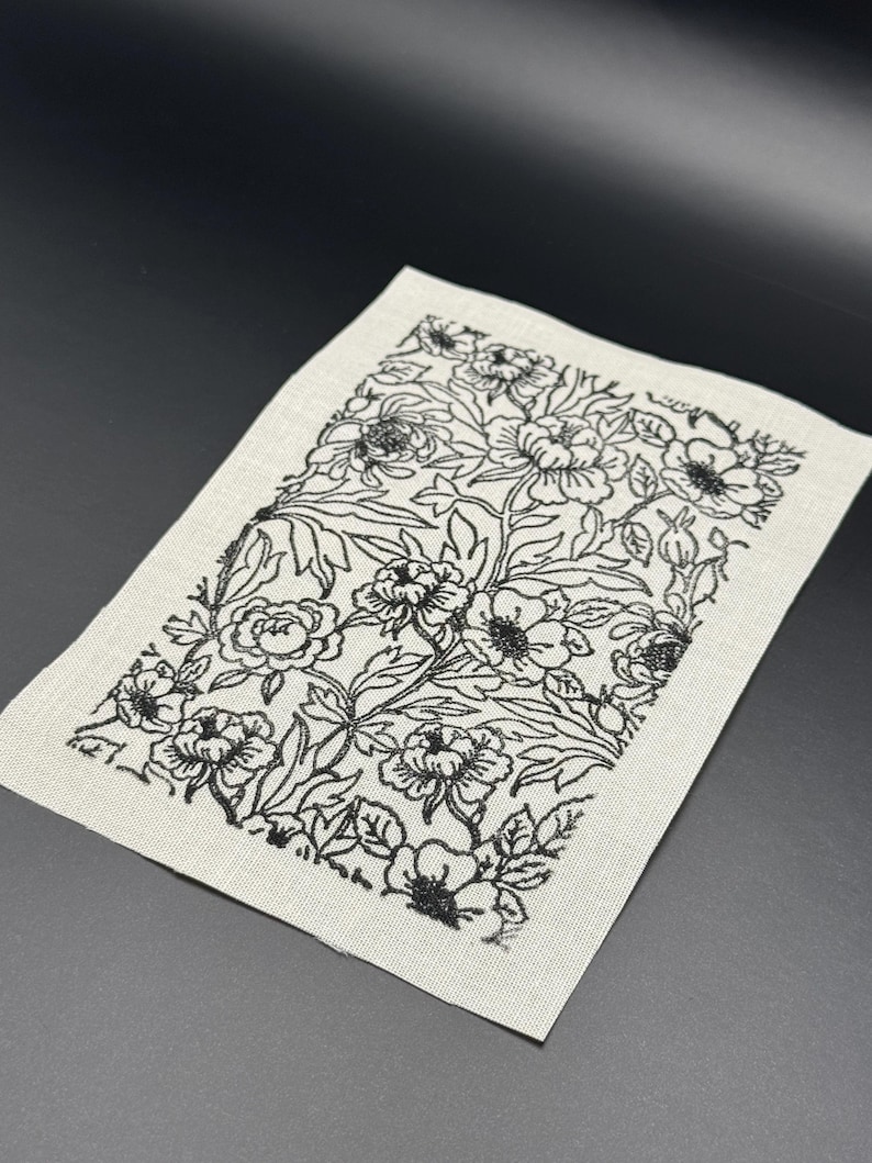Puede incluir: Una tela blanca con un estampado floral negro impreso en ella. El patr&oacute;n presenta una variedad de flores y hojas.