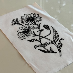 Könnte beinhalten: Schwarz-weiß-Zeichnung einer Blume mit drei Blüten und Blättern auf weißem Stoffhintergrund.