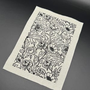 Puede incluir: Un parche de tela blanco con un dise&ntilde;o floral negro. El dise&ntilde;o presenta un patr&oacute;n repetitivo de flores y hojas.