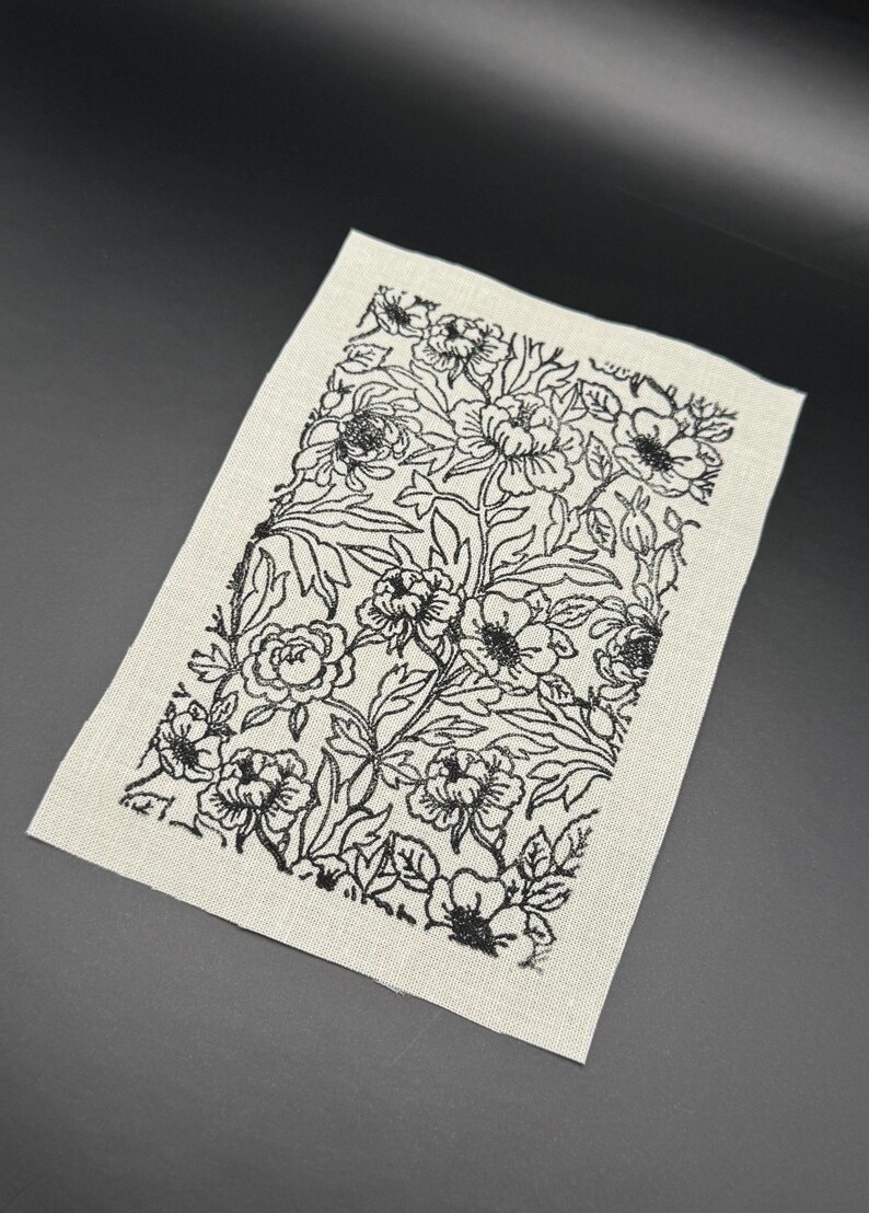 Puede incluir: Un parche de tela blanco con un dise&ntilde;o floral negro. El dise&ntilde;o presenta un patr&oacute;n repetitivo de flores y hojas.