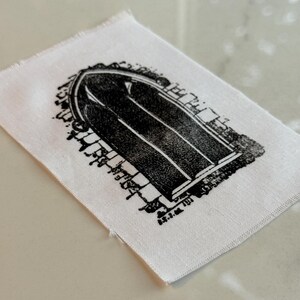 May include: A white fabric patch with a black and white print of an arched doorway.