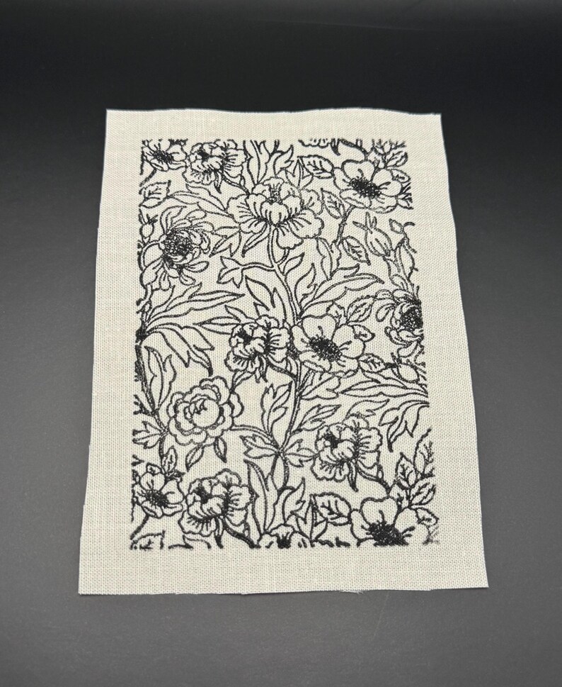 Puede incluir: Un parche de tela beige con un dise&ntilde;o floral negro. El dise&ntilde;o presenta un patr&oacute;n repetitivo de flores y hojas estilizadas.
