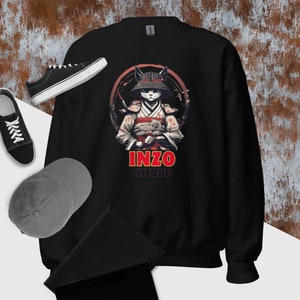 Może przedstawiać: Czarna bluza z nadrukiem stylizowanej ilustracji kota w stroju samuraja, trzymającego małego kota. Poniżej ilustracji znajduje się napis "INZO NITOBE". Na zdjęciu widoczne są również czarne trampki i szara czapka z daszkiem.