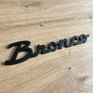May include: Black metal Bronco logo with a stylized script font.