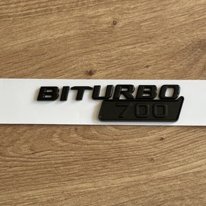 Puede incluir: Emblema Biturbo 700 en blanco y negro sobre fondo blanco.