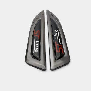 Op de afbeelding: Een paar grijze auto-emblemen met de tekst "ST-Line" in witte en rode letters.