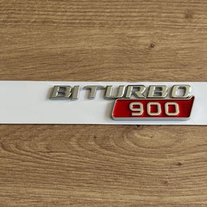 Puede incluir: Emblema de coche plateado y rojo con el texto "Biturbo 900".