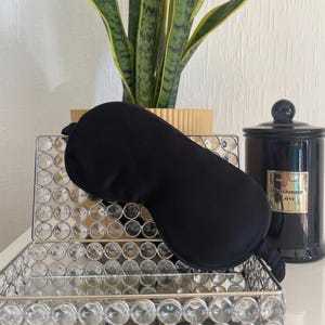 Peut inclure: Masque de sommeil en soie noire reposant sur un plateau argenté avec un motif décoratif de cercles. Le plateau est sur une surface en bois.