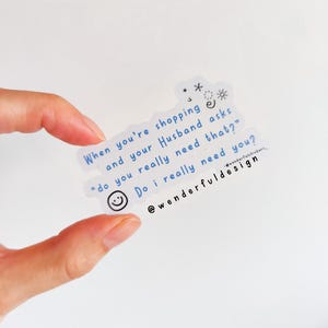 Può includere: Un adesivo bianco con testo blu che dice "Quando fai shopping e tuo marito ti chiede "Hai davvero bisogno di questo?" Ho davvero bisogno di te?" con una faccina sorridente e stelle. L'adesivo è su uno sfondo bianco.