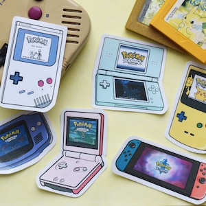 Può includere: Una collezione di nove adesivi per console di gioco Pokemon che presentano vari titoli di gioco, tra cui Pokemon Rosso, Pokemon Diamante, Pokemon Smeraldo e Pokemon Spada. Gli adesivi sono stampati su carta bianca con una finitura lucida e presentano illustrazioni colorate delle console di gioco.