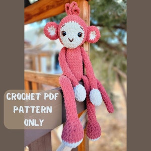 May include: Crochet pattern PDF for a red monkey amigurumi toy. The monkey is sitting on a wooden fence with its arms and legs outstretched.