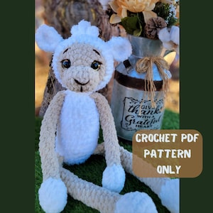 May include: Crochet pattern PDF for a white and beige plush lamb toy. The lamb is sitting on a green surface with a metal container behind it. The container has a sign that reads "Give thanks with a grateful heart."
