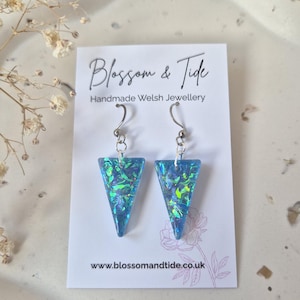 May include: A pair of blue and green triangle-shaped earrings with silver hooks. The earrings are on a white card with the text "Blossom & Tide Handmade Welsh Jewellery" and the website address.