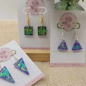 May include: Three pairs of iridescent earrings on display cards. The earrings are made of glass and have a variety of shapes, including squares and triangles. The cards are white with pink lettering that reads "Blossom & Tide Jeweller" and "Handmade in Wales".