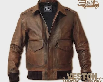 May include: Brown leather bomber jacket with two front pockets, a ribbed hem, and cuffs. The jacket has a collared neckline and a black interior. The text "Real Leather" is visible on a tag inside the jacket. The words "VESTON Leather Jackets" are written in a script font.