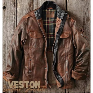 Op de afbeelding: Een bruin leren jack met een geruite voering en meerdere zakken. Het jack heeft een ritssluiting en een knoopsluiting aan de voorkant. De merknaam "VESTON" is zichtbaar aan de onderkant van het jack.