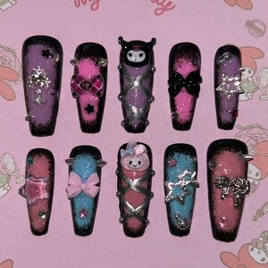 May include: A set of ten long, coffin-shaped press-on nails. Each nail features a unique design with a black and pink ombre effect, adorned with bows, stars, and character embellishments. The background reads "A sweet smile, a pretty Melody, My Melody."