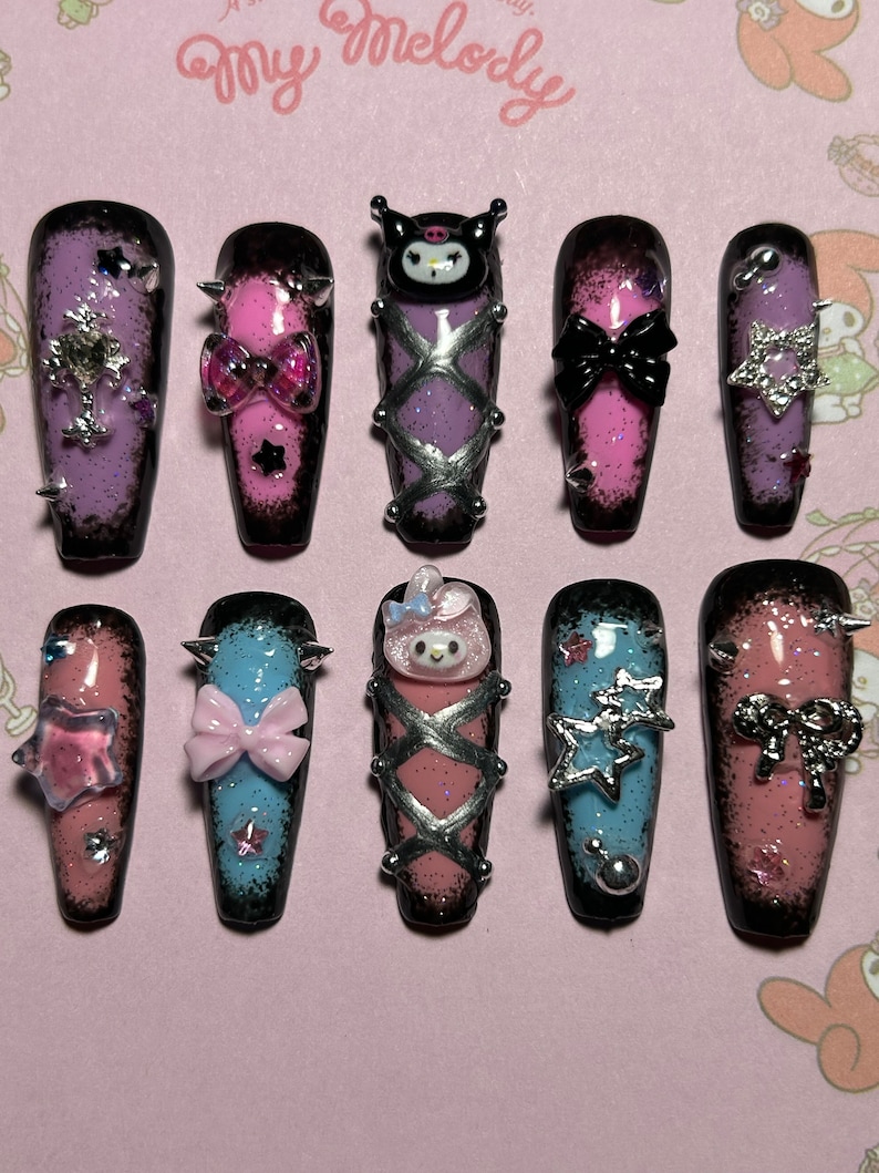 May include: A set of ten long, coffin-shaped press-on nails. Each nail features a gradient design with black tips and various embellishments, including bows, stars, and character designs. The nails are decorated with glitter and silver accents.