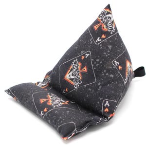 May include: A black and gray fabric tablet pillow with a playing card design featuring the Ace of Spades. The pillow has a triangular shape with a small loop on the side for easy handling.
