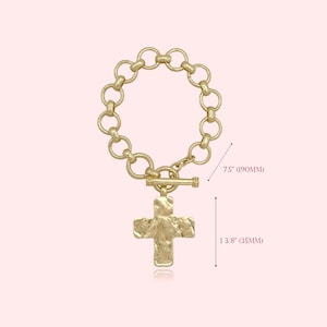 May include: Gold-toned bracelet featuring a textured cross pendant. The bracelet is 7.5 inches (190mm) long and the cross pendant is 1 3/8 inches (35mm) in length. The bracelet has a toggle clasp and a chain of connected circles.