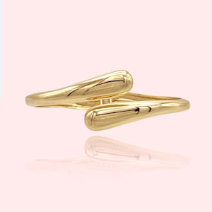 May include: A gold ring with a unique, twisted design. The ring is made of two smooth, rounded pieces of metal that are intertwined.